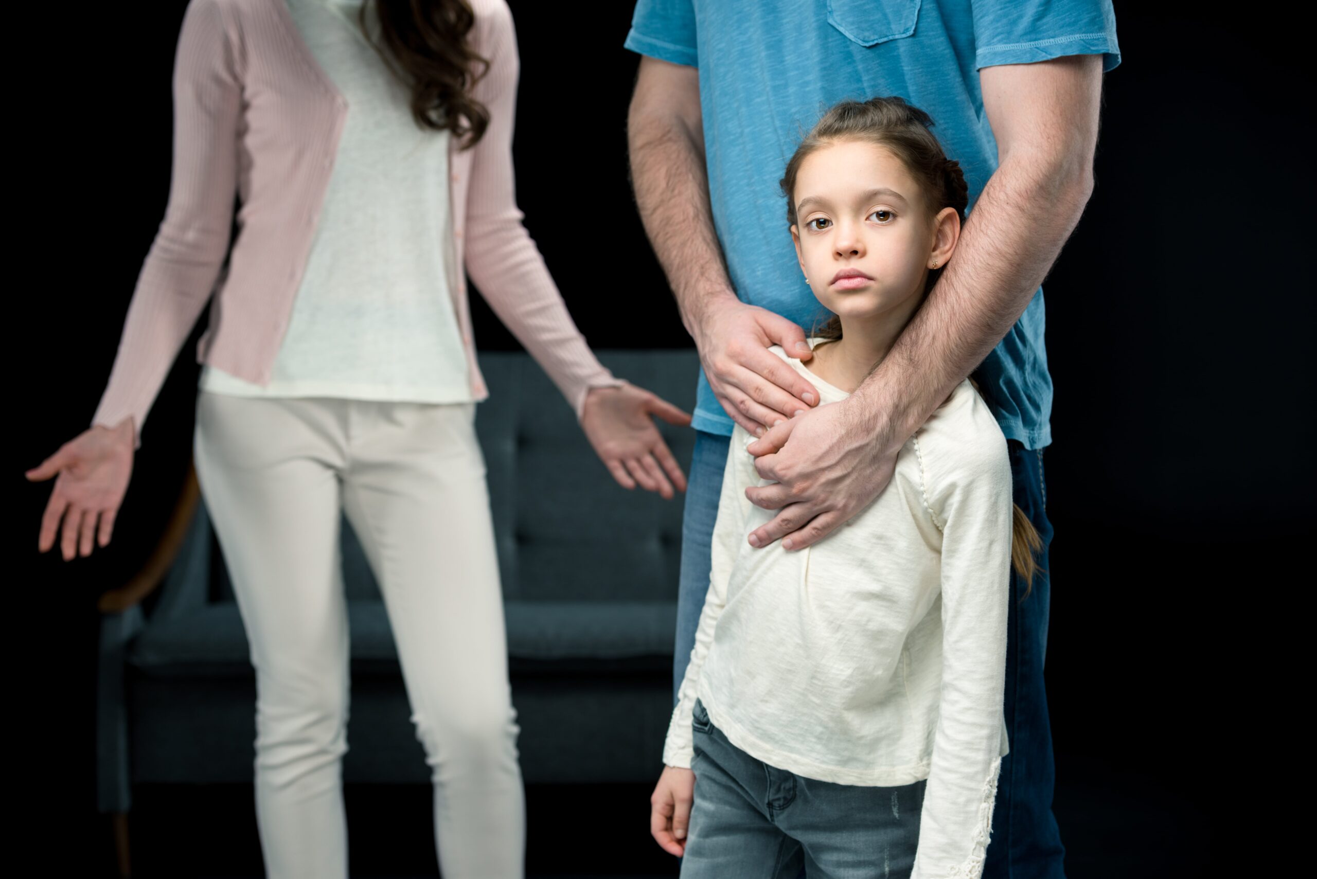 Father hugging daughter, mother in background, family custody scene